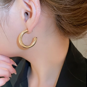 Close-up of golden C-shaped hoop earrings with hammered texture on a female model