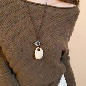 Close-up of a marble teardrop pendant with a circular ring on a brown knit sweater