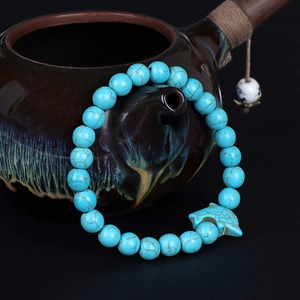 Turquoise stone bead bracelet with dolphin charm displayed on a dark ceramic teapot