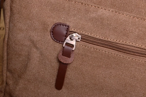 Close-up of brown canvas messenger bag with metal zipper and leather pull detail