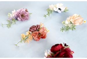 Five assorted colors of artificial bridal corsages with flowers and greenery accents