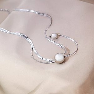 Detail of silver snake chain necklace featuring a white pearl over silk fabric
