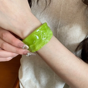 Close-up of a wide green acrylic resin bangle featuring a marble texture on a wrist