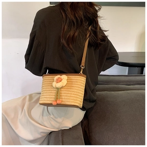 Detail of woven straw crossbody bag with floral pendant and brown leather trim