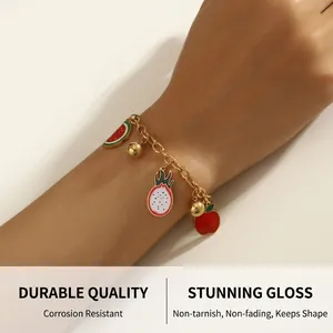 Close-up of gold chain bracelet featuring colorful enamel watermelon and dragon fruit charms
