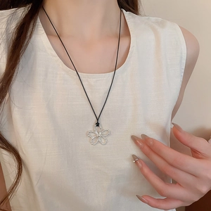 Gros plan d'un collier avec pendentif fleur évidée en argent sur un cordon noir élégant
