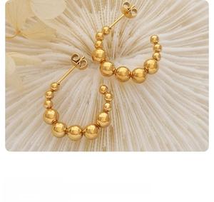 Détail de boucles d'oreilles créoles C dorées à billes dégradées sur texture de corail