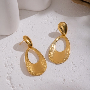 Macro shot of gold water-ripple textured oval drop earrings on elegant white setting