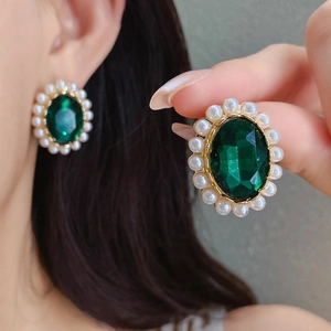 Detail of gold floral earrings with large green oval gemstones and pearl halo accents