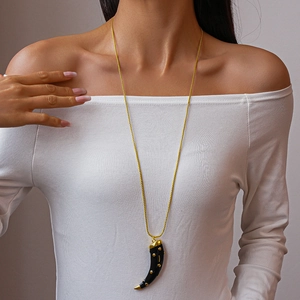 Detail of a black cornicello horn pendant with gold dots on a long chain necklace