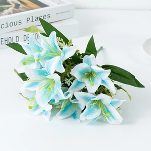 Artificial white lily bouquet with blue tips and green leaves on a white table