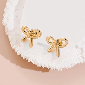 Detailed view of polished gold bow stud earrings on a textured white display tray