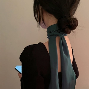 Detail view of a long dark green silk scarf tied elegantly around the neck, back view
