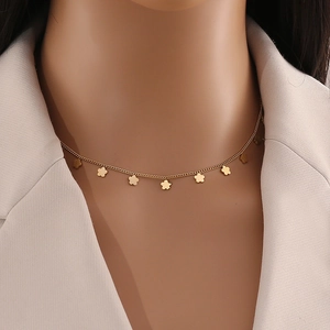 Macro view of gold flower pendant necklace worn on neck with white blazer
