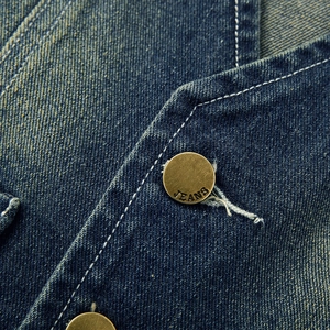 Dettaglio macro del tessuto denim lavato blu con bottone in rame vintage inciso JEANS