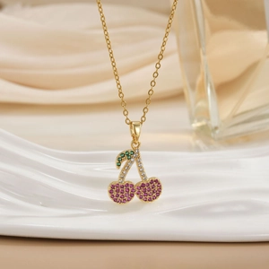Gold cherry pendant necklace with colorful rhinestones on a white wavy display stand