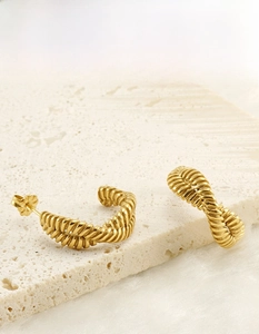 Detailed view of 18K gold plated twisted C-shape earrings on white stone and plush fabric
