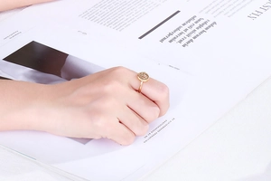 Minimalist gold-plated geometric ring shown on finger against a luxury magazine background