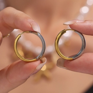 Minimalist 18K gold and silver two-tone stainless steel hoop earrings held in hand