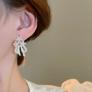 Close-up of elegant bow earrings with shimmering zircons and white pearlescent finish