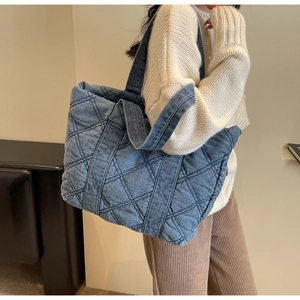 Vue détaillée d'un grand sac cabas en jean matelassé bleu porté par un mannequin à l'épaule