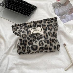 Detail of leopard print plush cosmetic bag with a woven tag on a soft white background
