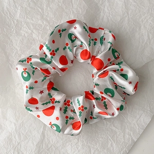 Detail of Christmas scrunchie with holly leaves and berry patterns on white satin