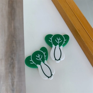 Macro detail of two green and white resin bok choy hair clips on a clean white surface