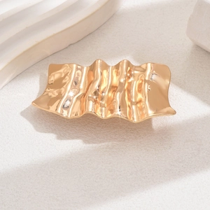 Close-up of golden irregular wavy textured metal hair clip on minimalist stone background