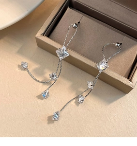 Detail shot of silver tassel earrings with geometric crystals resting on a jewelry box