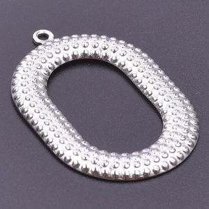 Macro detail of oval stainless steel pendant with textured dot pattern and top ring