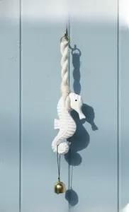 Detail of hand-carved white wooden seahorse wall hanging with golden bell and cotton rope