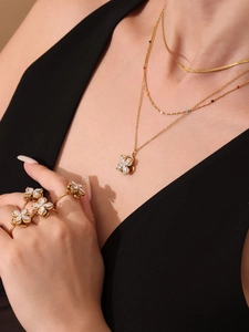 Close-up of model wearing gold clover necklace and rings with zircon stones