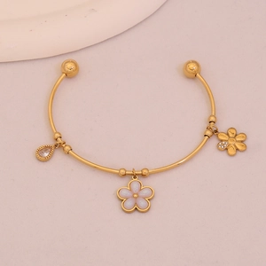 Detail of gold open bangle with white flower, heart drop, and zircon charms