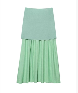 Détail d'un gilet en tricot vert menthe et d'un ensemble jupe plissée assortie sur fond blanc