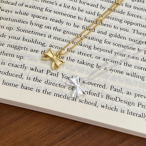 Detailed view of silver and gold bow necklaces with bead chains on a vintage book