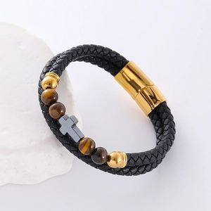 Pulsera de cuero trenzado con cuentas de ojo de tigre y colgante de cruz sobre piedra
