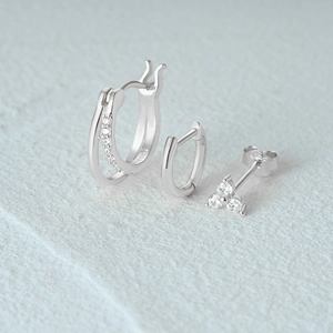 Detail of S925 sterling silver earring set featuring hoops and a three-stone stud earring