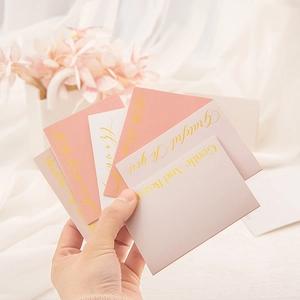 Close-up of hand holding pink and white gold-foiled greeting cards with floral background