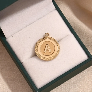 Macro shot of 18K gold-plated striped round pendant with letter A on green velvet