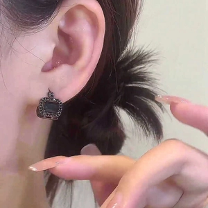 Detailansicht von quadratischen Vintage-Ohrringen im dunklen Stil mit Strass am Ohr.