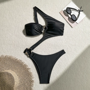 Detail of black one-shoulder swimsuit featuring cut-outs and golden metal rings on a beach mat