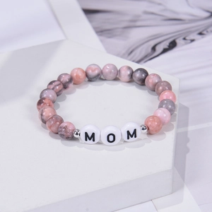 Macro detail of 8mm pink zebra stone beads with MOM letter beads on a white platform
