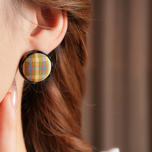 Detailed close-up of model wearing green plaid fabric round button earrings with black rim