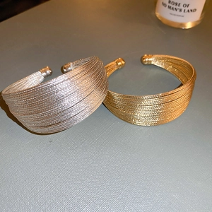 Dettaglio di bracciali a polsino multistrato oro e argento con estremità sferiche
