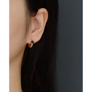 Close-up of golden hoop earrings with black round stone inlay on a female model's ear