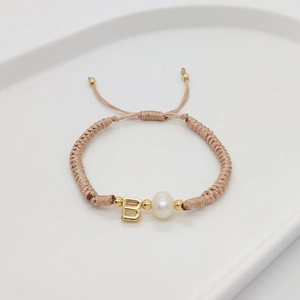 Detail of woven bracelet with letter B bead and freshwater pearl on white ceramic tray