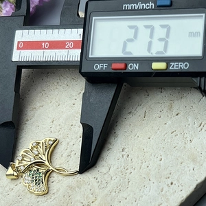Macro view of gold ginkgo leaf pendant with zircon stones being measured by a digital caliper