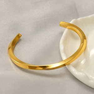 Detailed view of a gold-plated twisted C-shaped open bangle on a ceramic tray