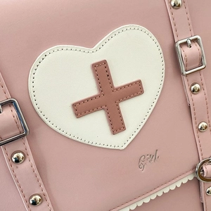 Detail of pink leather bag featuring a white heart patch and adjustable silver buckle